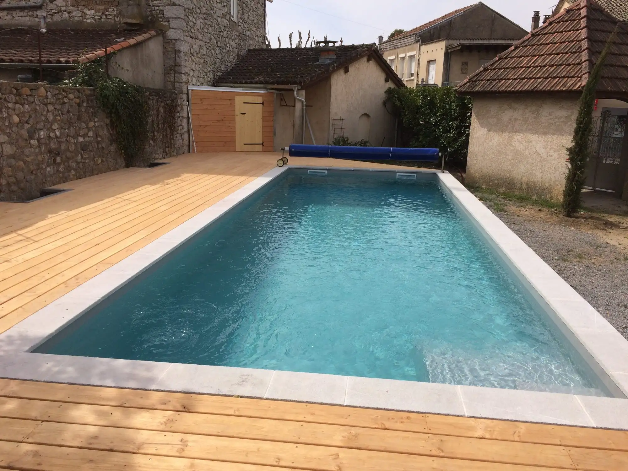 Piscine turquoise dans une cour de village en pierre à Ruoms
