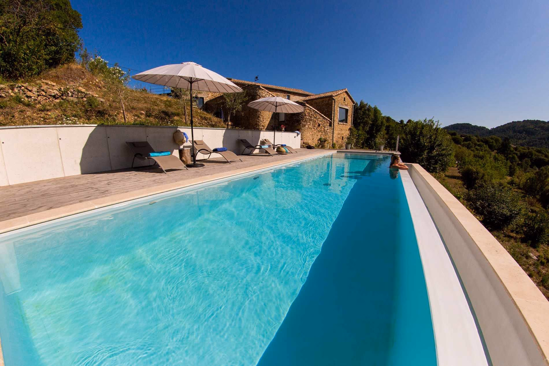 Piscine à débordement le long d'une terrasse, maison en pierre en surplomb, à Chassiers
