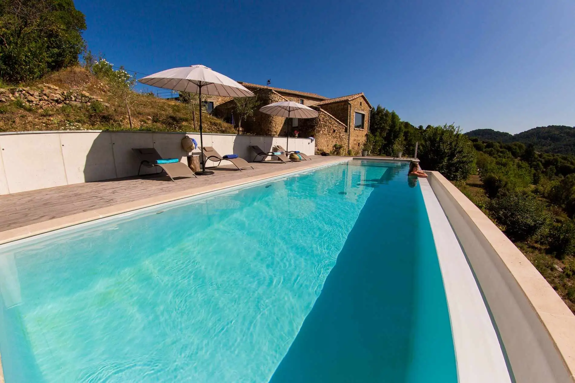 Piscine à débordement le long d'une terrasse, maison en pierre en surplomb, à Chassiers