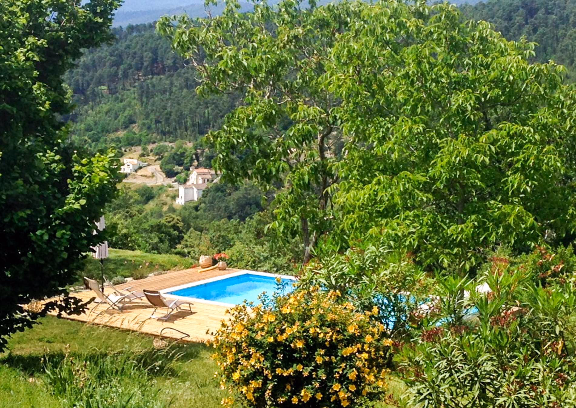 Piscine et terrasse en bois au milieu de la végétation, vue sur le village, à Largentière