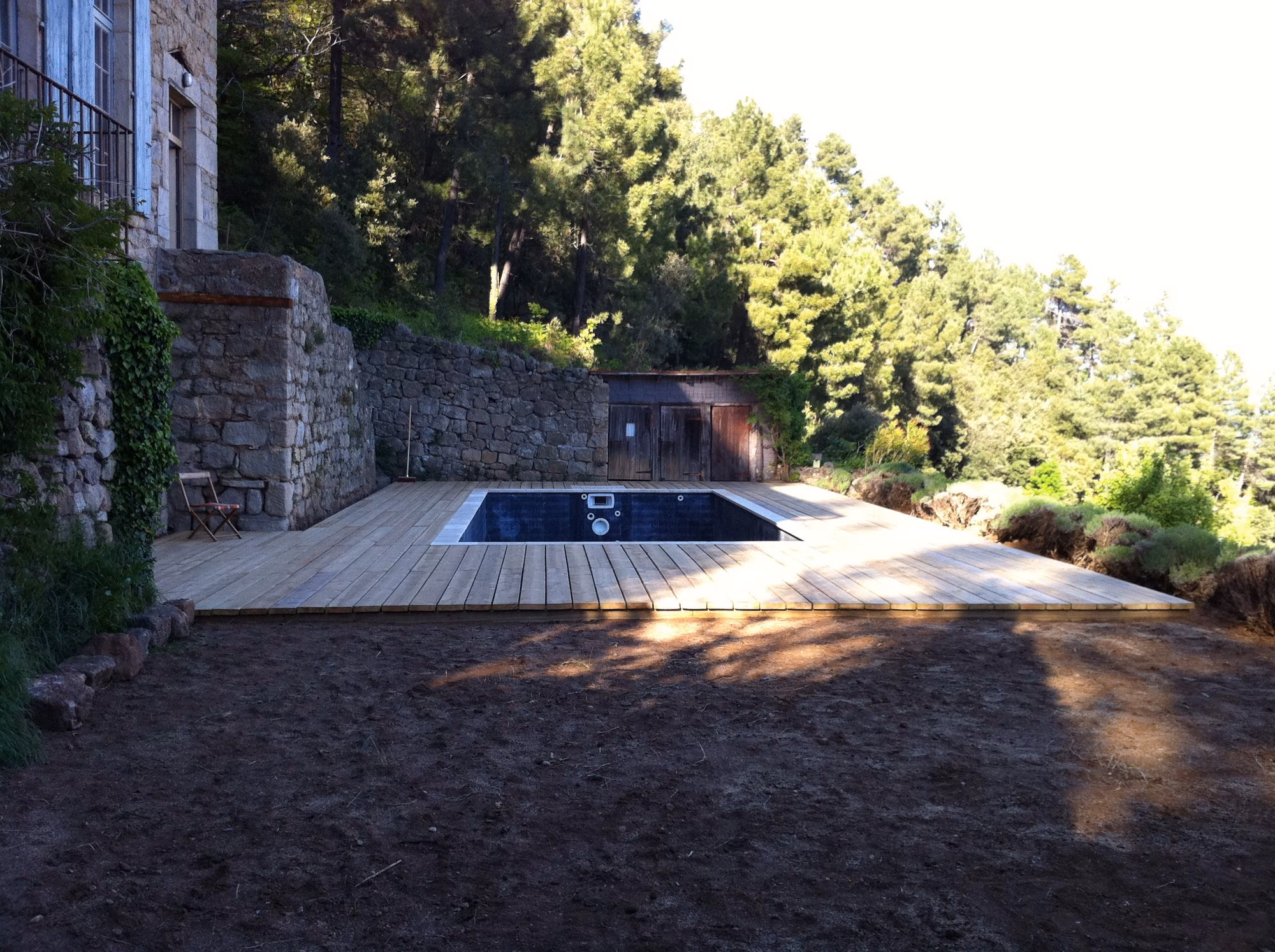Piscine noire et terrasse bois au pied d'une bâtisse en pierre à Sanilhac