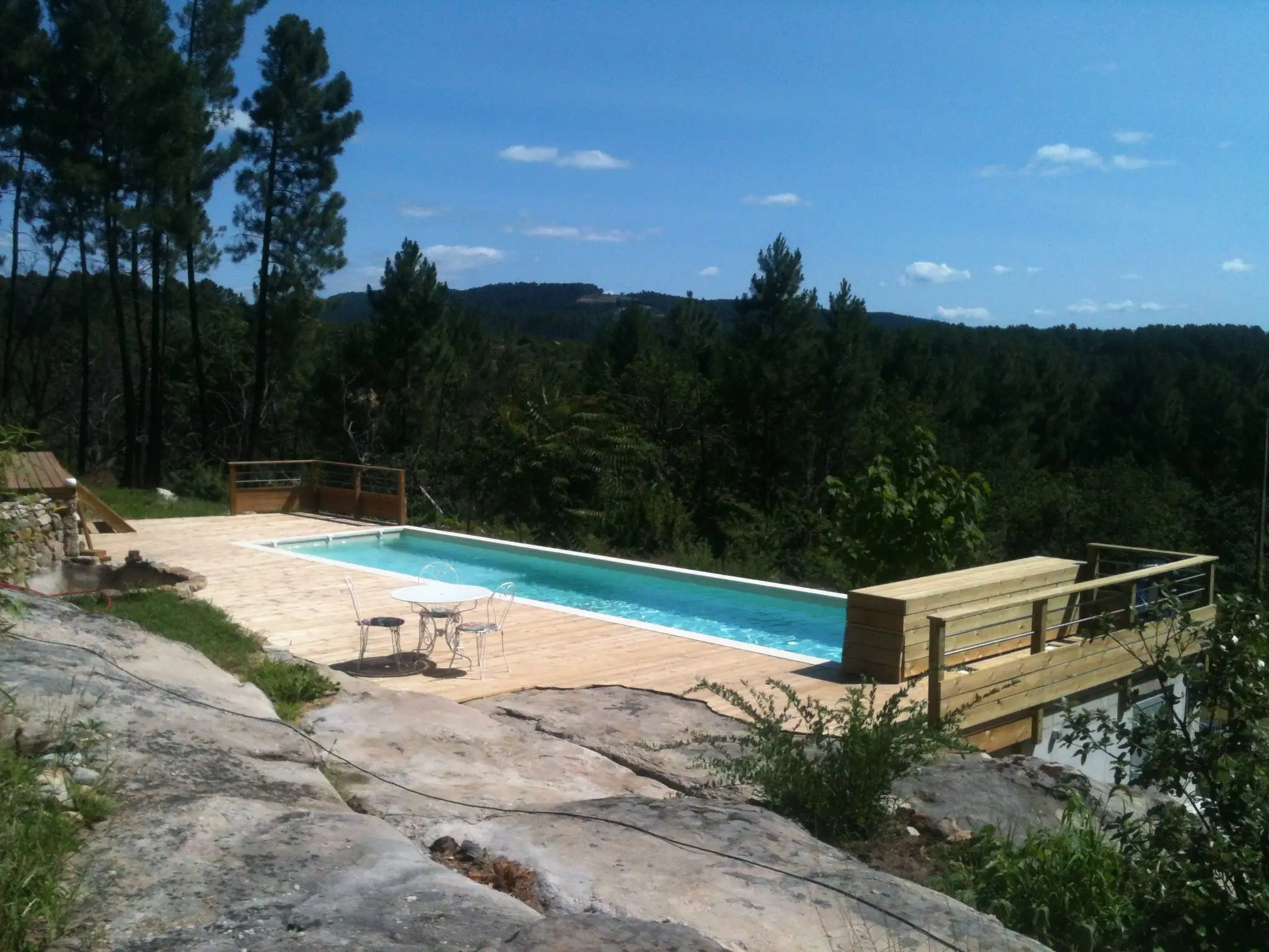 Couloir de nage en béton banché et terrasse en bois posés sur un rocher, face à la forêt