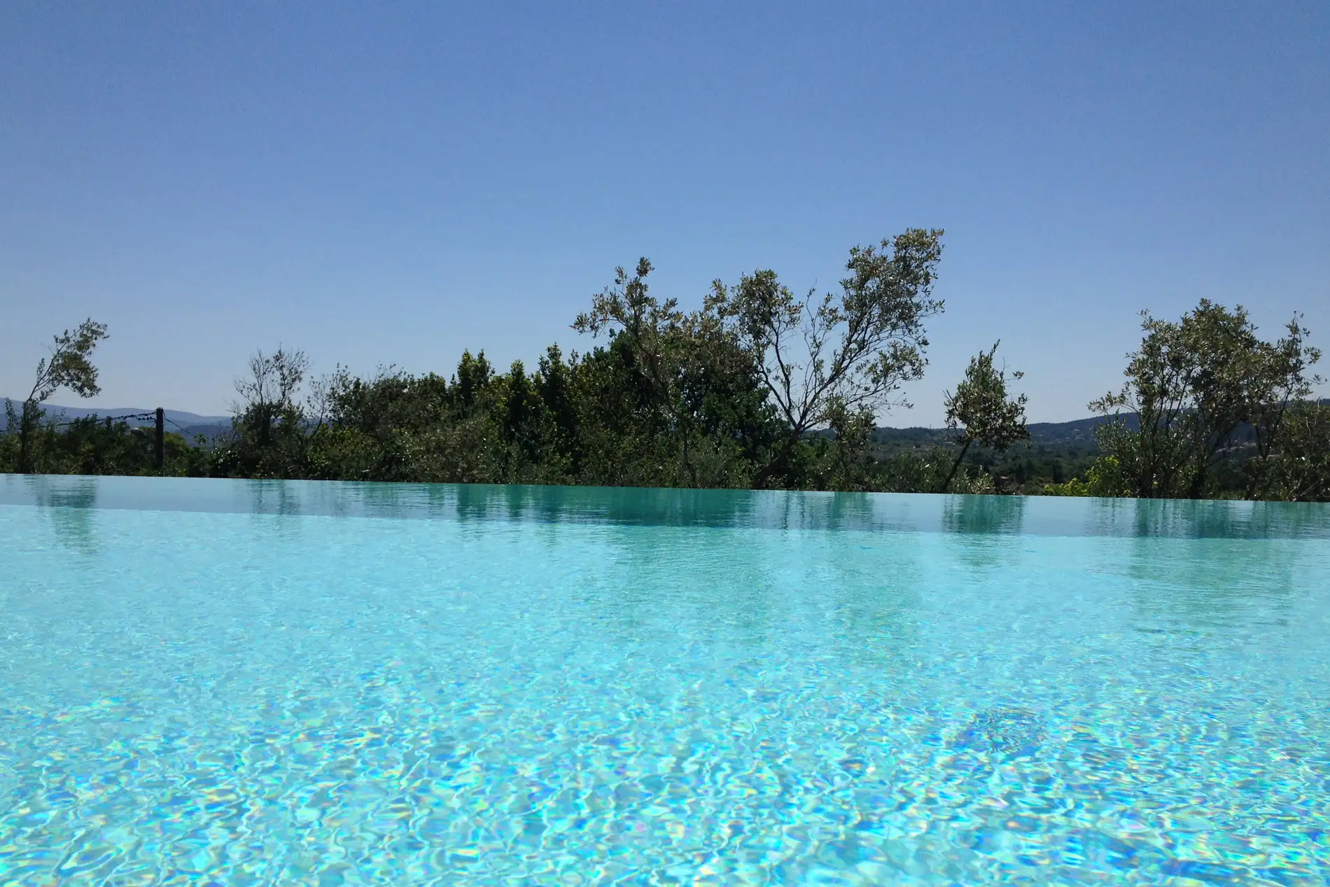 Piscine à débordement en Ardèche, ligne d'eau prolongée par les arbres et le ciel