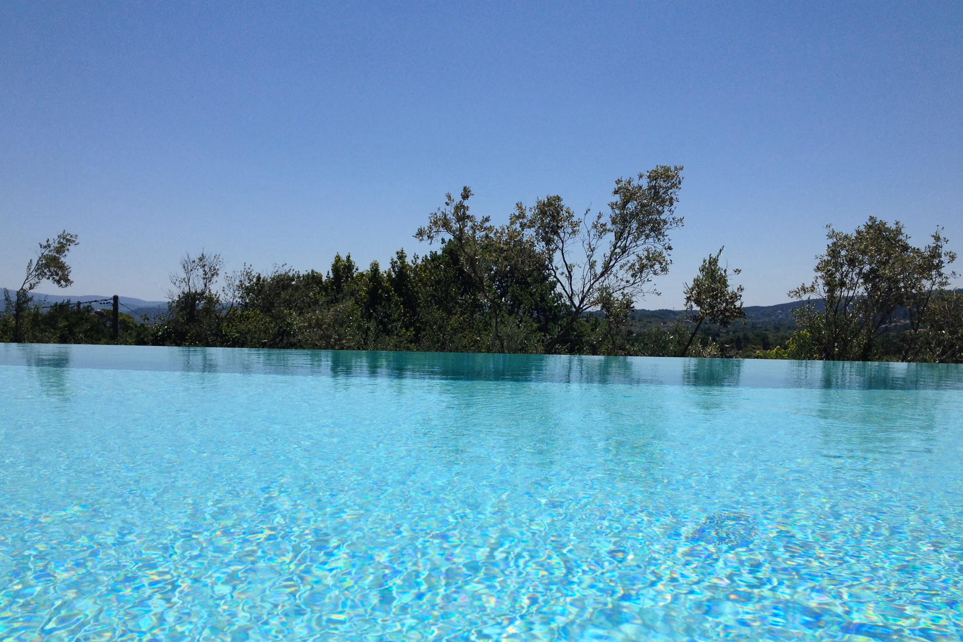 Piscine à débordement en Ardèche, ligne d’eau prolongée par les arbres et le ciel