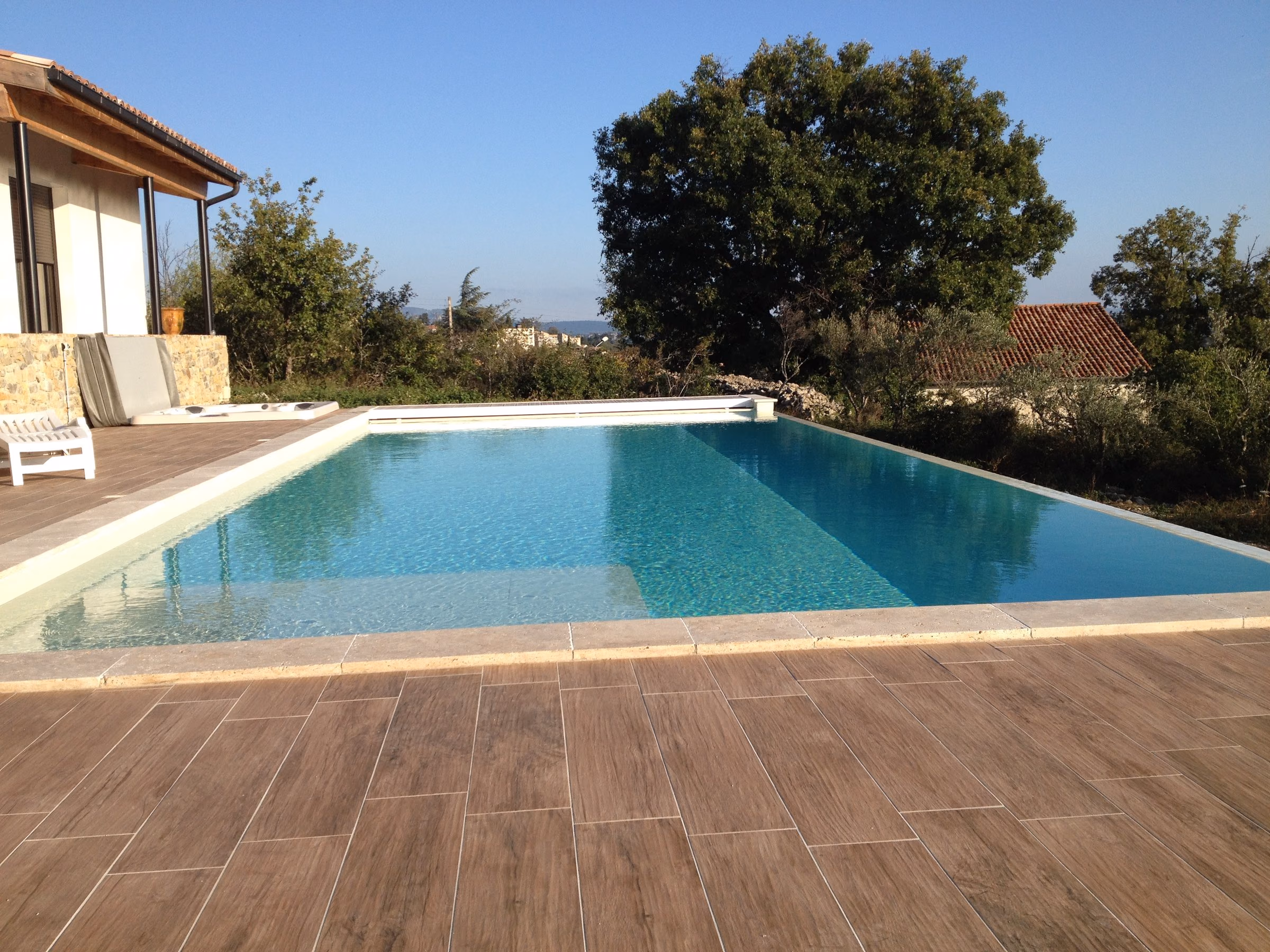 Plage en carrelage effet bois et lame d'eau d'une piscine à débordement, face aux collines