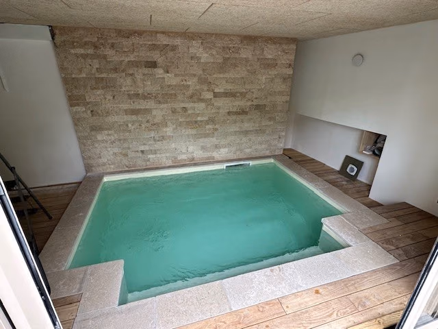 Petite piscine intérieure à angles en escalier, mur de pierre et plage en bois