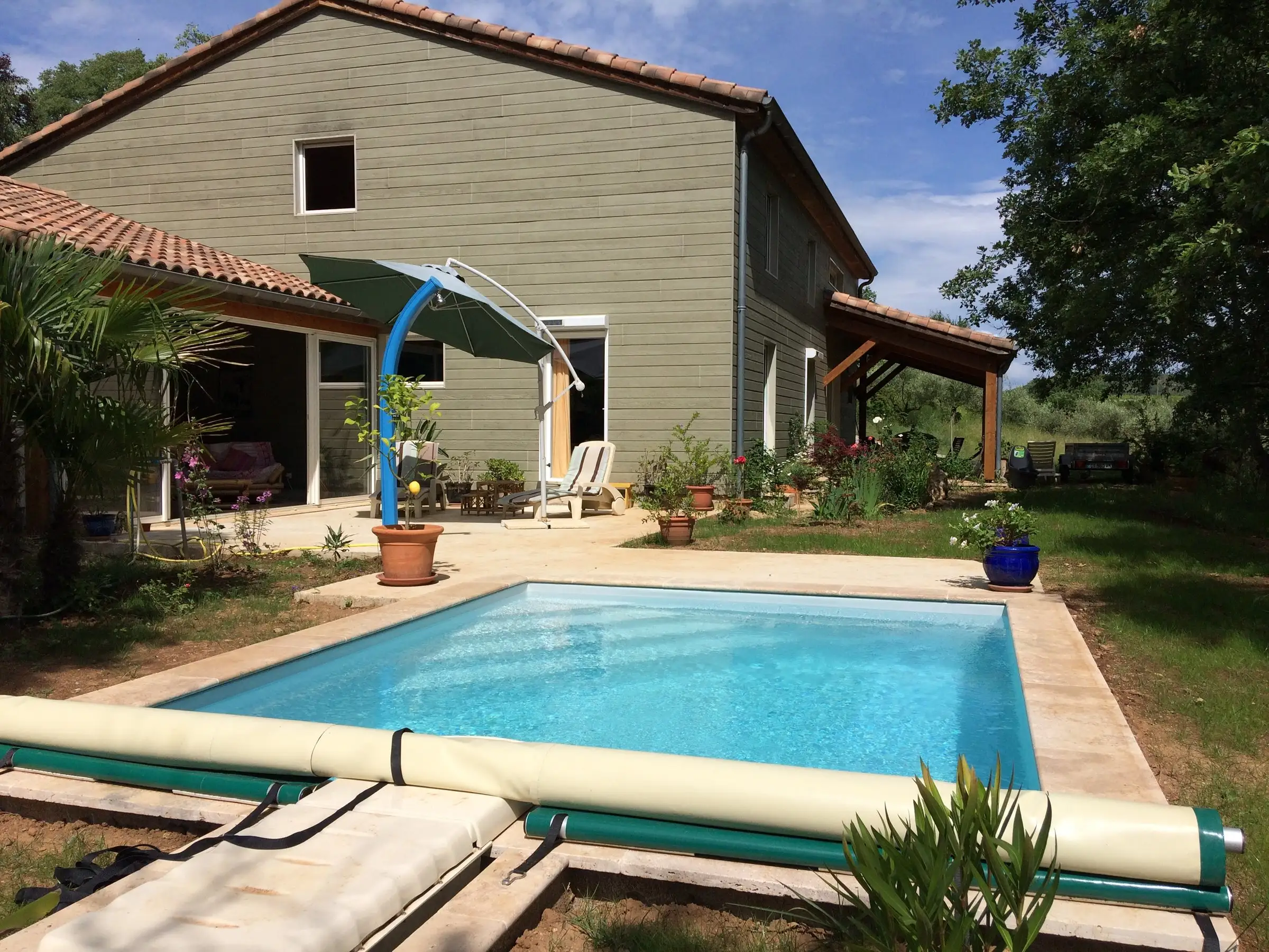 Douche solaire au bord d'une piscine, devant la terrasse couverte d'une maison