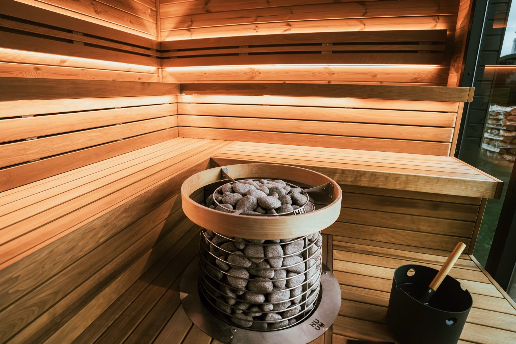 Intérieur de sauna en bois clair, banquettes et poêle à pierres